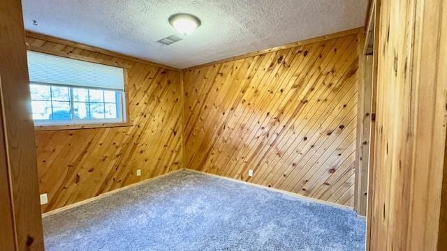 unfurnished room with carpet floors, a textured ceiling, and wooden walls