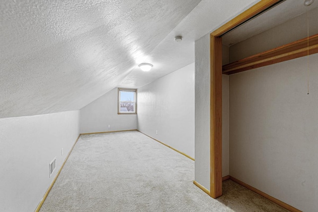 additional living space with lofted ceiling, light carpet, and a textured ceiling