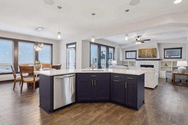 kitchen featuring sink, stainless steel dishwasher, decorative light fixtures, a fireplace, and a center island with sink