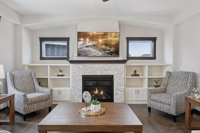 living area featuring dark wood-style floors, vaulted ceiling, and a stone fireplace