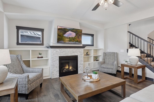 living area with dark wood-style floors, a ceiling fan, a fireplace, and stairs