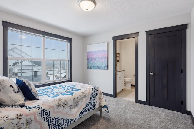 bedroom with a textured ceiling, light carpet, ensuite bathroom, and baseboards