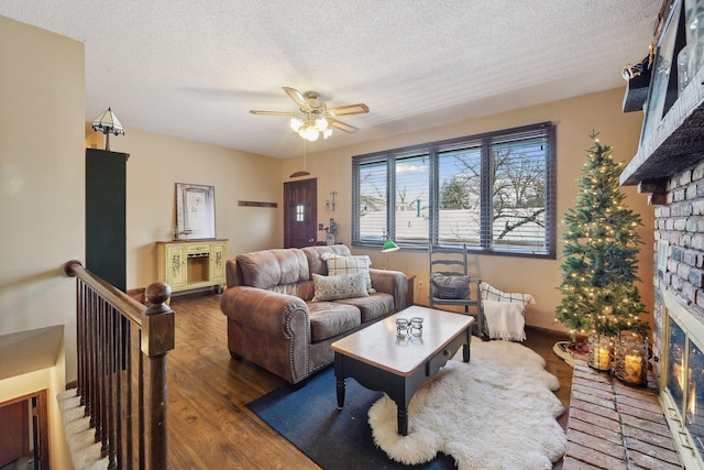 living room featuring ceiling fan, dark wood-type flooring, a textured ceiling, and a brick fireplace