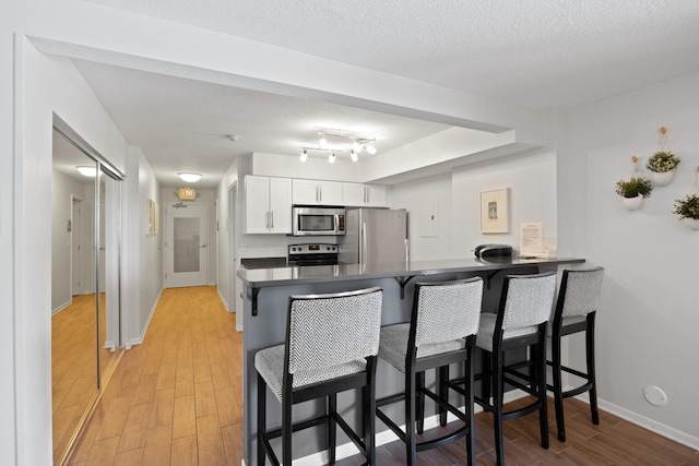 kitchen with stainless steel appliances, light hardwood / wood-style floors, white cabinets, a kitchen bar, and kitchen peninsula