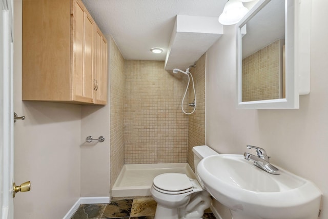 bathroom with sink, tiled shower, and toilet