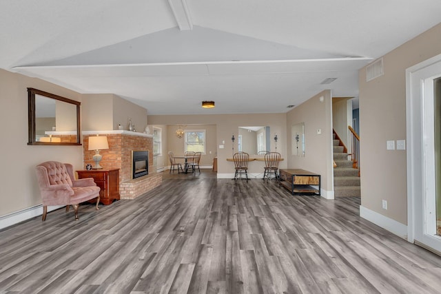 living room with vaulted ceiling with beams, light hardwood / wood-style floors, and a brick fireplace