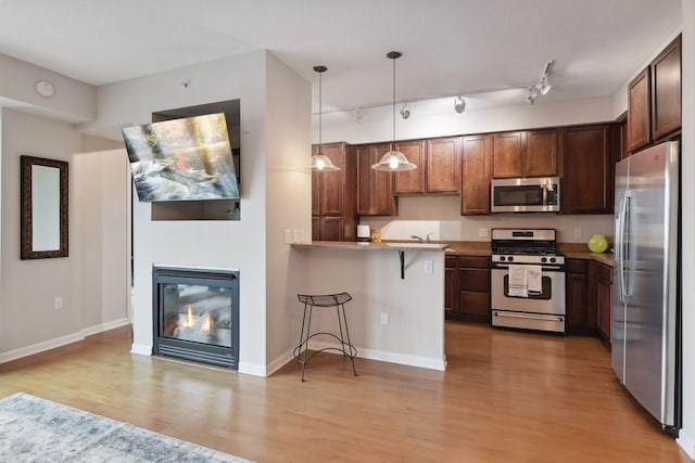 kitchen with kitchen peninsula, track lighting, decorative light fixtures, a breakfast bar, and appliances with stainless steel finishes