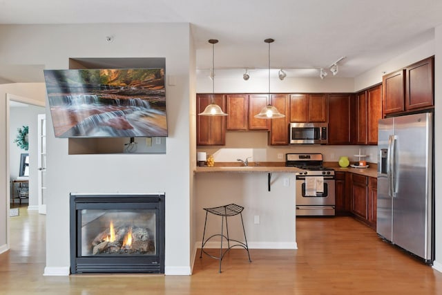 kitchen with rail lighting, hanging light fixtures, stainless steel appliances, light hardwood / wood-style flooring, and a kitchen bar