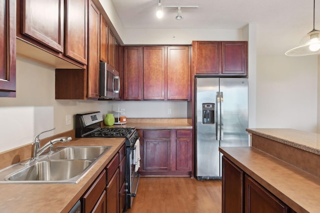 kitchen with appliances with stainless steel finishes, light wood-type flooring, pendant lighting, and sink