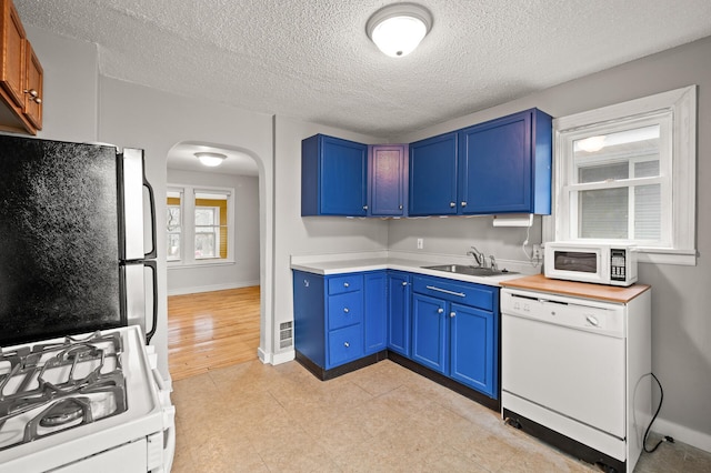 kitchen with light wood-type flooring, a textured ceiling, white appliances, blue cabinets, and sink