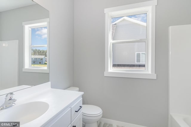 bathroom featuring a washtub, vanity, a healthy amount of sunlight, and toilet