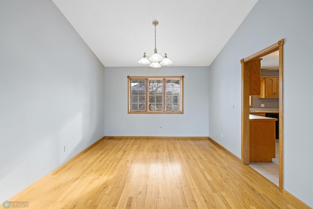 unfurnished dining area with a chandelier, vaulted ceiling, a textured ceiling, and light hardwood / wood-style flooring