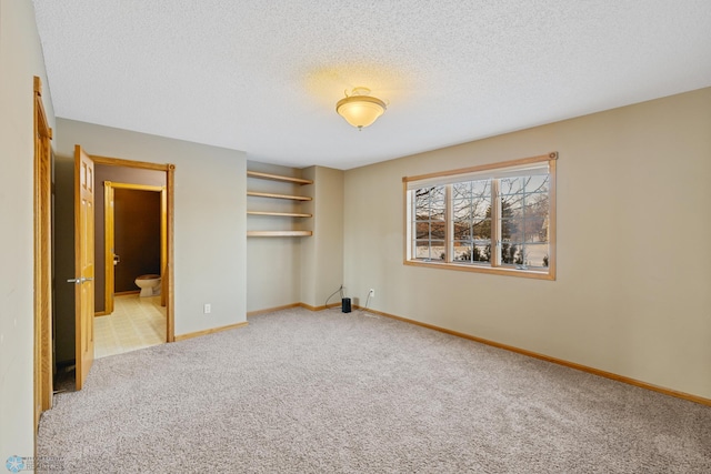 unfurnished bedroom with a textured ceiling, light carpet, and connected bathroom