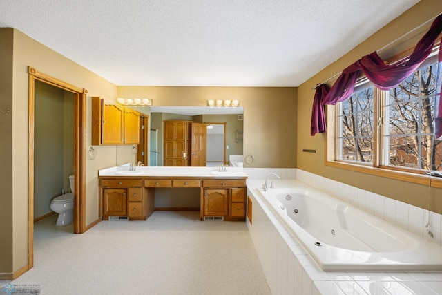 bathroom with vanity, a textured ceiling, a relaxing tiled tub, and toilet