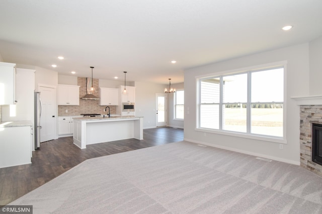 kitchen featuring wall chimney exhaust hood, dark wood-type flooring, stainless steel appliances, a center island with sink, and white cabinets