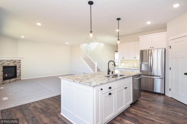 kitchen with white cabinetry, sink, stainless steel appliances, a stone fireplace, and a center island with sink