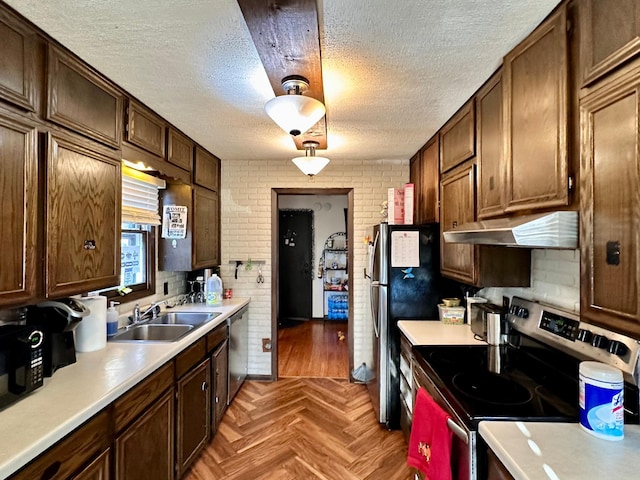 kitchen with appliances with stainless steel finishes, brick wall, a textured ceiling, sink, and light parquet flooring