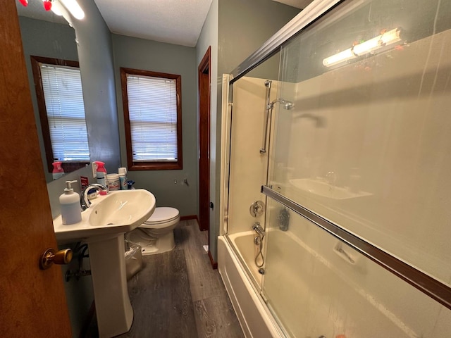 bathroom with wood-type flooring, toilet, and bath / shower combo with glass door