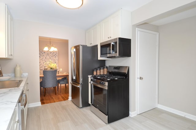 kitchen with light stone countertops, white cabinetry, stainless steel appliances, a notable chandelier, and light hardwood / wood-style floors