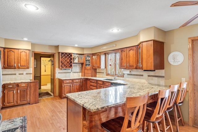 kitchen featuring backsplash, sink, light hardwood / wood-style flooring, a kitchen bar, and kitchen peninsula