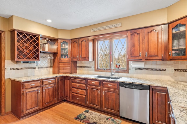 kitchen with light stone countertops, backsplash, stainless steel dishwasher, sink, and light hardwood / wood-style flooring