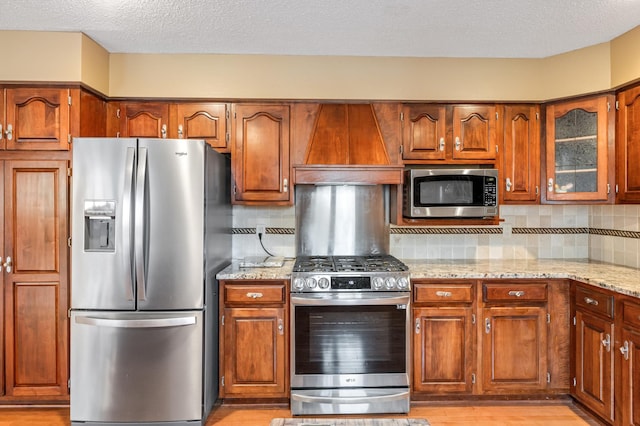 kitchen featuring tasteful backsplash, light hardwood / wood-style floors, light stone counters, custom range hood, and stainless steel appliances