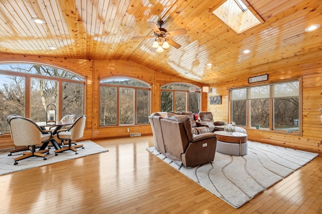 living room featuring vaulted ceiling with skylight, wood walls, wood ceiling, and light hardwood / wood-style floors