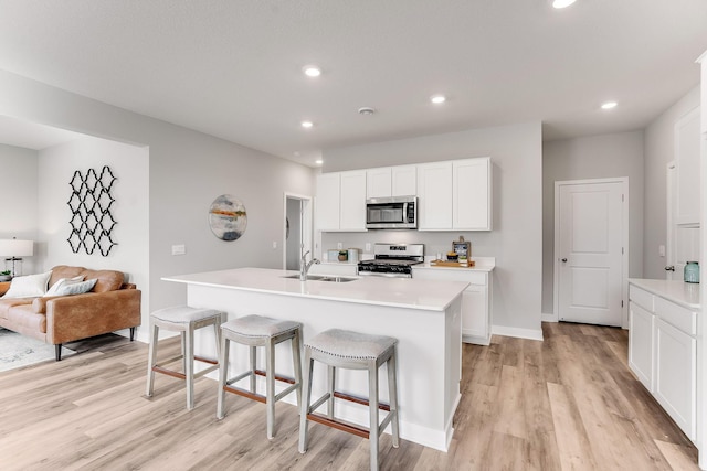 kitchen with a center island with sink, sink, light wood-type flooring, gas range gas stove, and white cabinetry