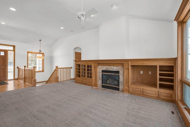 unfurnished living room with ceiling fan, lofted ceiling, light carpet, and a tile fireplace