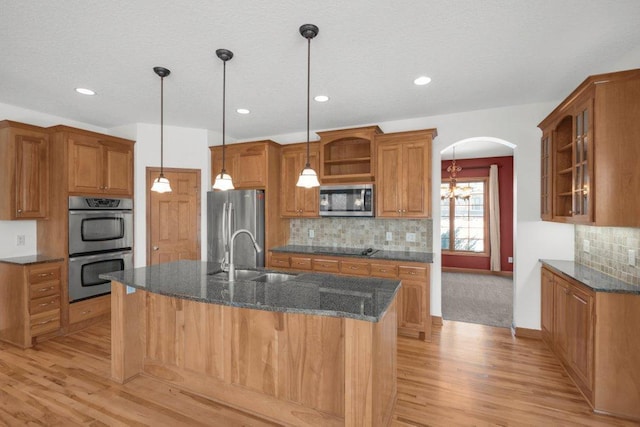 kitchen featuring appliances with stainless steel finishes, light wood-type flooring, dark stone countertops, and sink