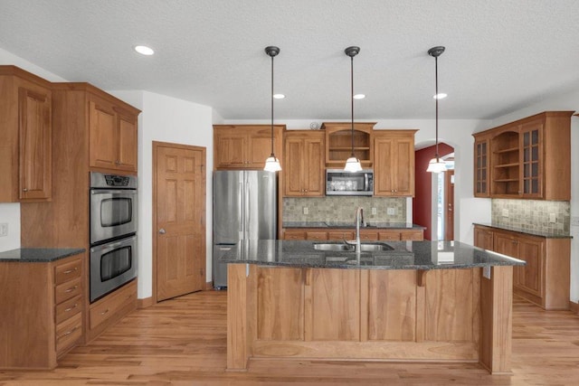 kitchen featuring sink, an island with sink, decorative light fixtures, light hardwood / wood-style floors, and stainless steel appliances