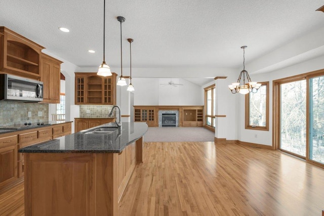 kitchen with sink, hanging light fixtures, tasteful backsplash, light hardwood / wood-style floors, and a kitchen island with sink