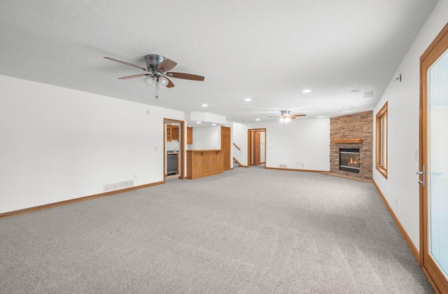 unfurnished living room featuring carpet flooring, ceiling fan, and a stone fireplace