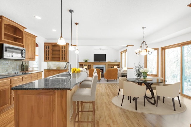 kitchen with decorative backsplash, light wood-type flooring, ceiling fan with notable chandelier, sink, and pendant lighting