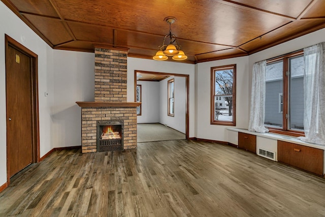 unfurnished living room with ornamental molding, hardwood / wood-style flooring, wooden ceiling, a notable chandelier, and a fireplace