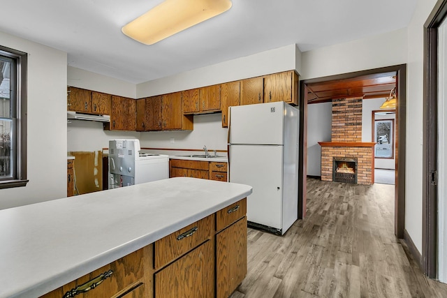 kitchen with light wood-type flooring, white appliances, a brick fireplace, and sink