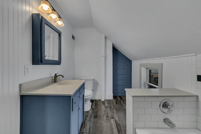 bathroom featuring hardwood / wood-style floors, vanity, lofted ceiling, a washtub, and toilet