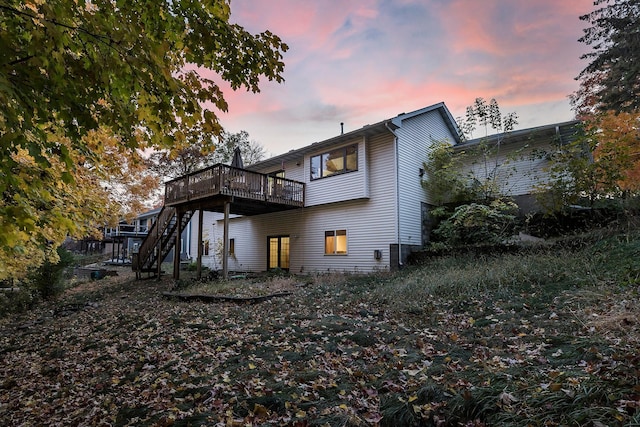 back of house at dusk featuring stairway and a wooden deck