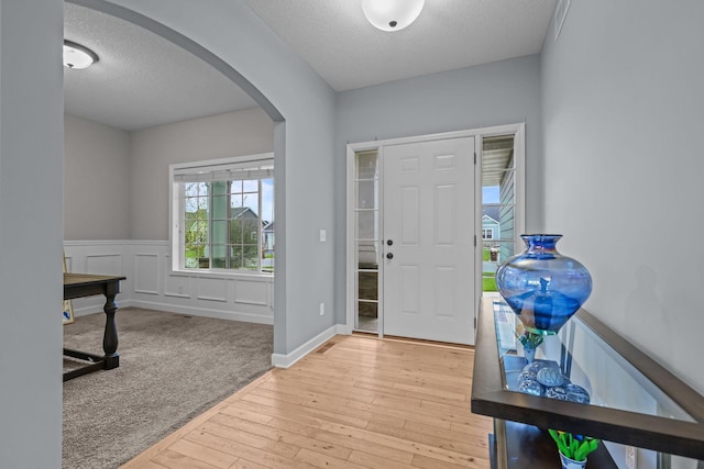 entryway with arched walkways, a textured ceiling, wainscoting, and light wood-style flooring