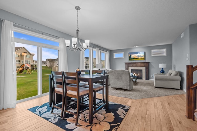 dining room with a healthy amount of sunlight, light wood finished floors, a tile fireplace, and a chandelier