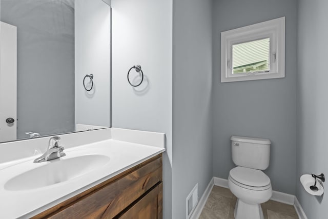 half bathroom with tile patterned flooring, vanity, toilet, baseboards, and visible vents