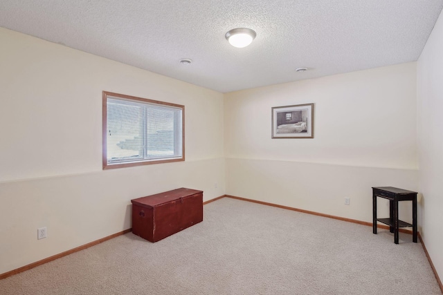 spare room with light carpet, baseboards, and a textured ceiling