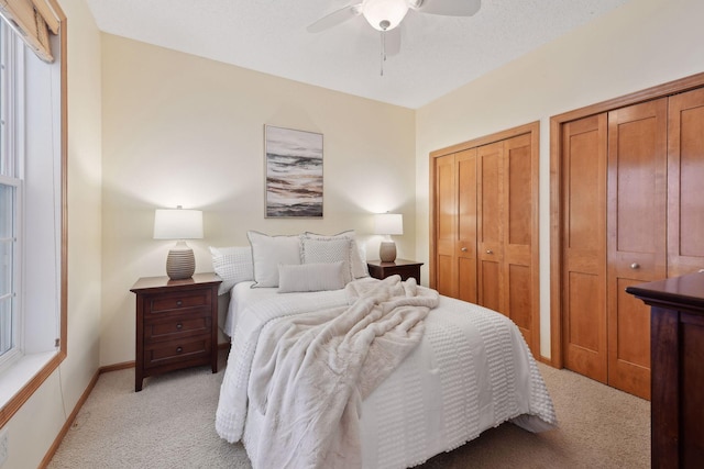 bedroom featuring light carpet, two closets, a ceiling fan, and baseboards