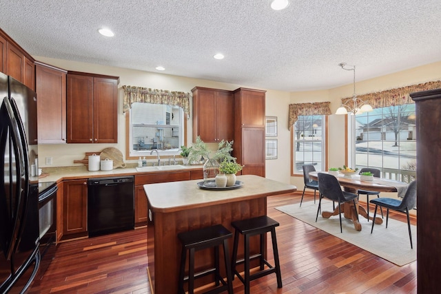 kitchen with black appliances, a kitchen island, light countertops, and decorative light fixtures