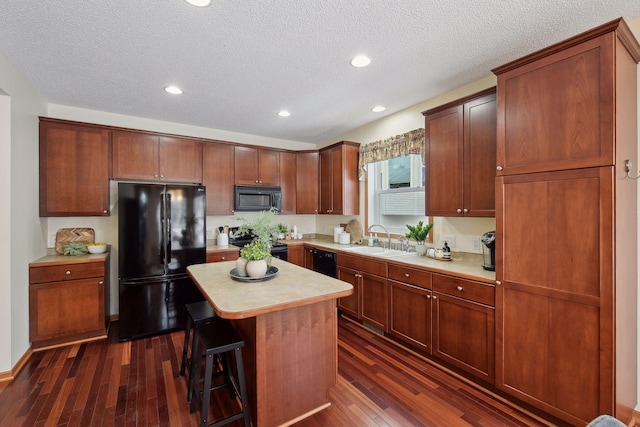 kitchen featuring a breakfast bar, a center island, light countertops, black appliances, and a sink