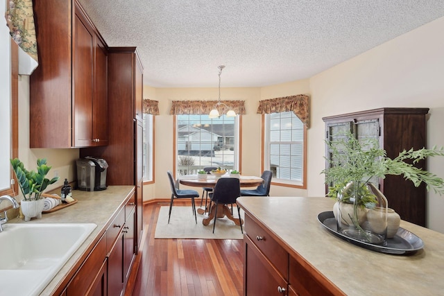 kitchen with a textured ceiling, dark wood-style flooring, a sink, light countertops, and decorative light fixtures