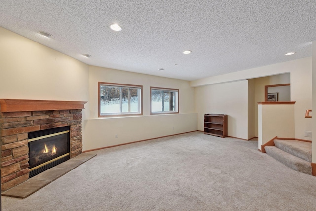 unfurnished living room with light carpet, a textured ceiling, a stone fireplace, baseboards, and stairs