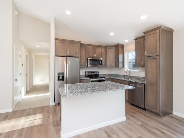 kitchen with light stone countertops, stainless steel appliances, sink, light hardwood / wood-style flooring, and a kitchen island