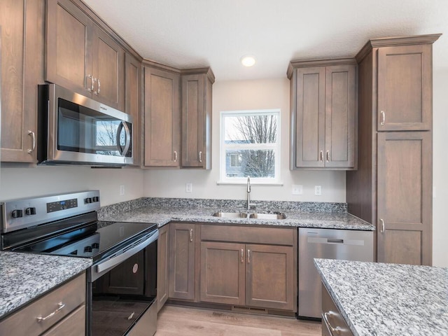 kitchen with light wood-type flooring, stainless steel appliances, light stone counters, and sink