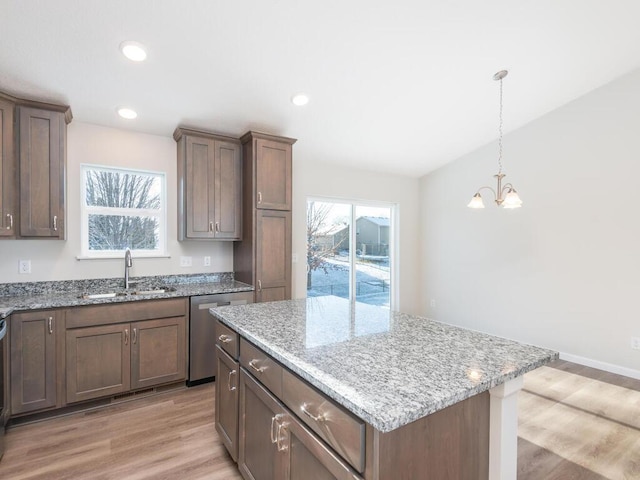 kitchen with sink, stainless steel dishwasher, a kitchen island, light stone countertops, and light hardwood / wood-style floors